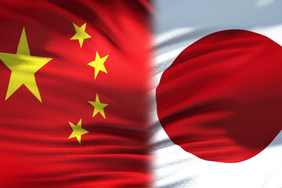 Primer plano de dos banderas ondeando unidas en el centro: a la izquierda, la bandera de China con fondo rojo y cinco estrellas amarillas en la esquina superior izquierda; a la derecha, la bandera de Japón con fondo blanco y un gran círculo rojo en el centro. Ambas telas muestran pliegues y textura, simbolizando la relación y vínculo entre ambos países asiáticos.